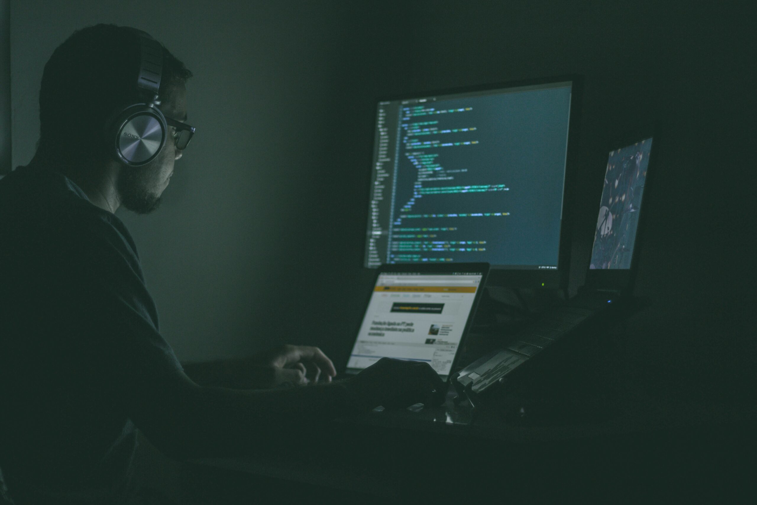 A person working in a dark room with a computer displaying lines of code, representing a digital workspace.